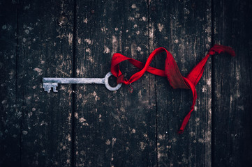 an antique rusty key on red ribbon on vintage wooden board