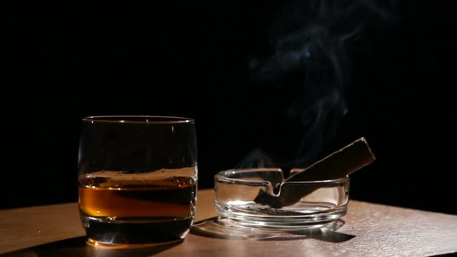 Glass of whiskey with smoking cigar.Glass of alcohol and smoking noble cigar on a black background.Rotating glasses of whiskey.