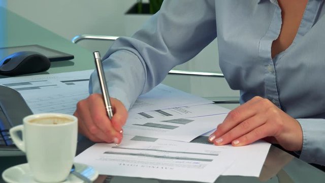 A woman writes on papers in an office - closeup on the hands