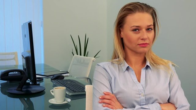 A young, beautiful woman sits at a desk in an office, looks at the camera and shakes her head
