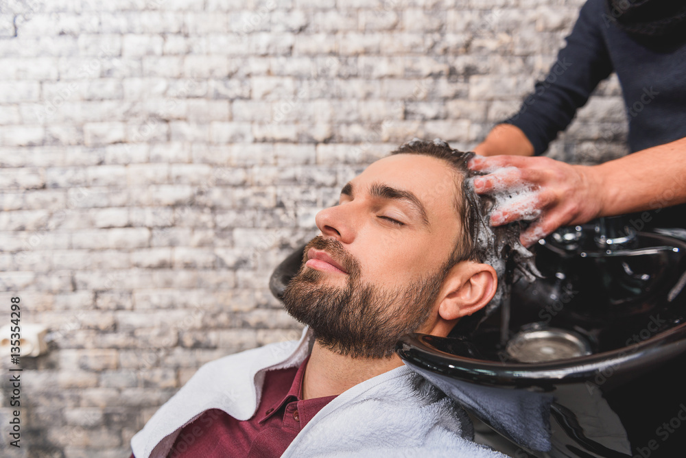 Wall mural young man enjoying hairwash at beauty salon