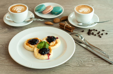 Cheesecakes for breakfast with jam and cappuccino coffee. Top view of a wooden background.