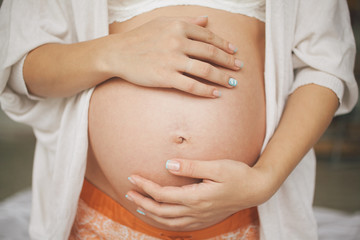 Close up foto of pregnant caucasian woman holding her hands on baby bump.