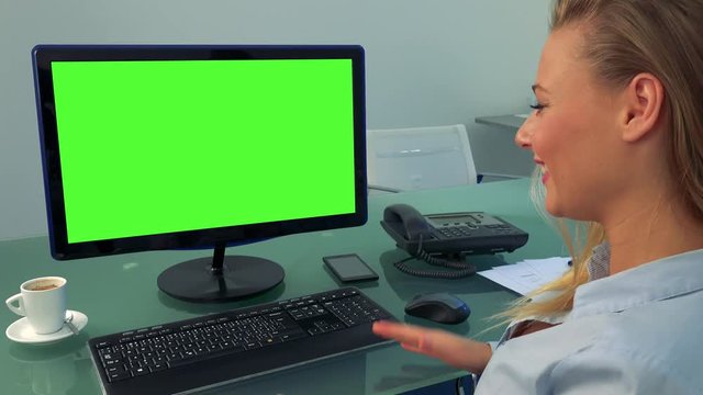 A young, beautiful woman sits in front of a computer with a green screen in an office and celebrates