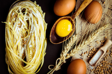 Pasta, eggs and wheat spikes on a white wooden background