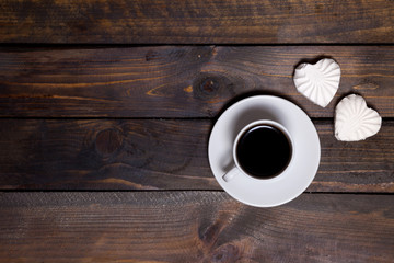 White mug of coffee and two marshmallows in the shape of hearts on a wooden background for breakfast
