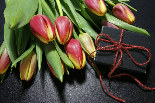 bouquet of tulips and gift box on black background