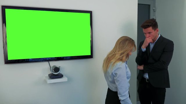 A man and a woman stand beside a green television screen, upset