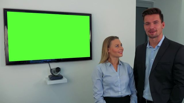 A man and a woman (both young and attractive) stand beside a green television screen and talk to the camera