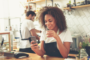 Smiling bartender drinking coffee and keeping phone in hand