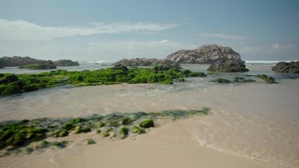 Waves beat against mossy rocks on shore of the Atlantic ocean in Portugal. Beauty and power of nature concept.