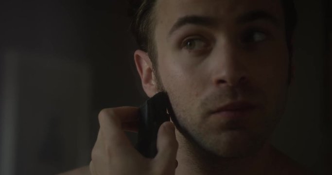 Slow motion shot of a White man shaving his sideburns in the mirror.