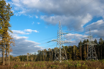 Obraz premium Poles with high-voltage electrical wires on a background of forest and blue sky with clouds.