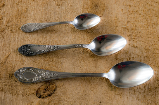 Three silver spoons of various sizes on a background of wooden boards with texture.