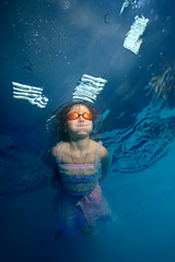 Beautiful little girl swims underwater in a beautiful gown and looks up. Portrait. Shooting under...