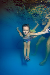 Fototapeta na wymiar The little girl dives under water surrounded by bubbles, and mom helps her. Portrait. Shooting under the water surface. Vertical orientation