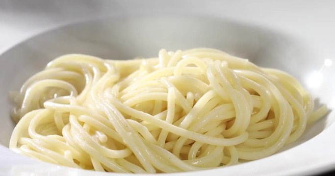 Serving cooked Italian spaghetti pasta spooning it onto a clean white generic plate in a closeup view on the noodles