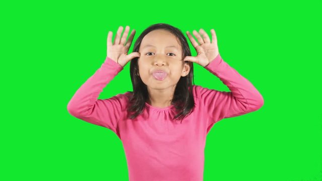 Funny little girl showing a silly face expression in the studio with green background