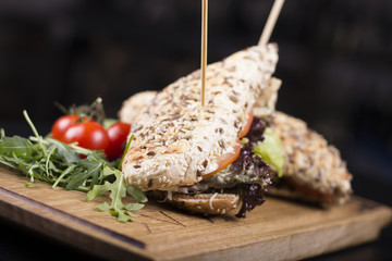 Delicious sandwiches, tomatoes, and french fries. Pickles and lettuce dripping off the side. Barbecue stick stabbed through the sandwiches on a wooden table.
