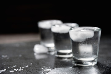 Vodka shots with ice cubes on black stone,
