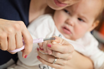 Obraz na płótnie Canvas Mother cutting fingernails of her nine months old baby girl