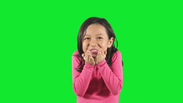 Cute little girl blowing a kiss at the camera in the studio with green background