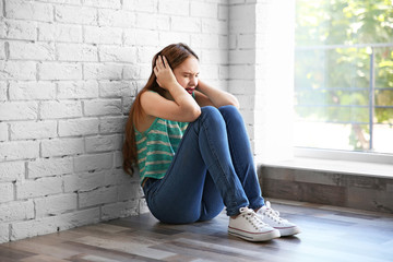 Sad teenage girl sitting near window in a room