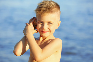 Obraz premium Cute boy listening to seashell on sea background