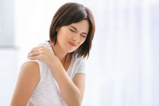 Beautiful young woman suffering from pain in shoulder at home