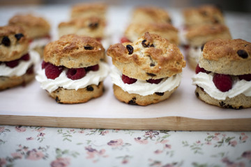 Fruit scones with cream and raspberries on a wooden board on a floral tablecloth