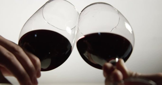 Isolated low angle slow motion shot of two red wine glasses tapping to cheers.