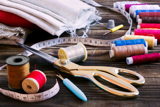 sewing tools, multi-coloured fabric and threads on a wooden background