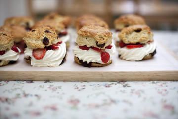 Fruit scones with cream and raspberries on a wooden board on a floral tablecloth