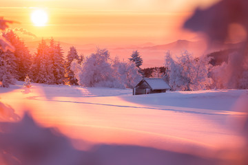 Golden sunlight over a idyllic white winter landscape with a little wooden hut in background
