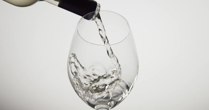 Isolated low angle slow motion shot of a glass filling with white wine.