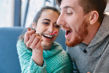 couple eating a dessert in a cafe on a date and drinking coffee. woman and man looks at a spoon with cake and smiling. Love story and Valentines.