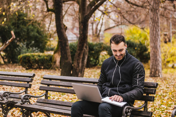 Fototapeta premium Young businessman with laptop sitting on bench at park
