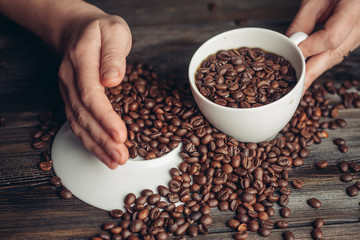 Coffee beans on a light saucer and a cup in hand