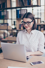 Portrait of smart female manager in glasses typing on laptop