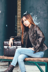 Fototapeta na wymiar Fashionable girl sitting on the bench with leather bag