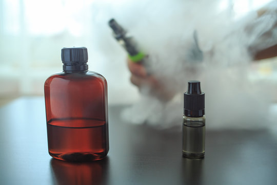 The bottle of flavor for personal vaporiser and other bottles stand on a black wooden table. A lot of steam.
