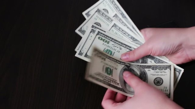 Women's hands holding a fan of hundred dollar bills and counts