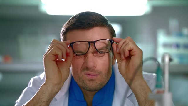 Scientist remove glasses from face. Scientist looking at glasses. Man holds glasses in hands. Portrait of lab man thinking in laboratory. Scientist in lab. Researcher thinking. Closeup lab worker