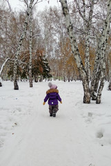 Fototapeta na wymiar Child in lilac winter clothes walking in winter park