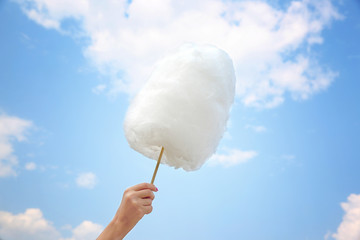 Female hand holding cotton candy on blue sky background