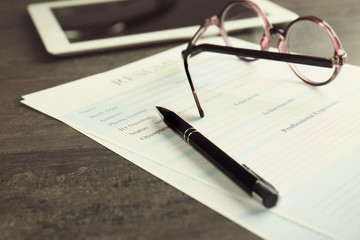 Resume, eyeglasses and pen on grey table, closeup