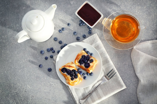 Sweet tasty pastries with bilberries on plate and cup of tea, top view