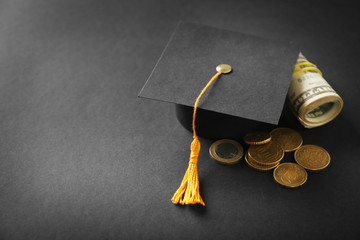 Graduation hat, dollar banknotes and coins on dark table. Pocket money concept