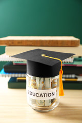 Glass jar with money for education on wooden table against green background