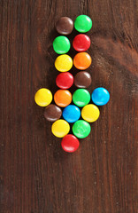 Arrow made of colorful candies on wooden background